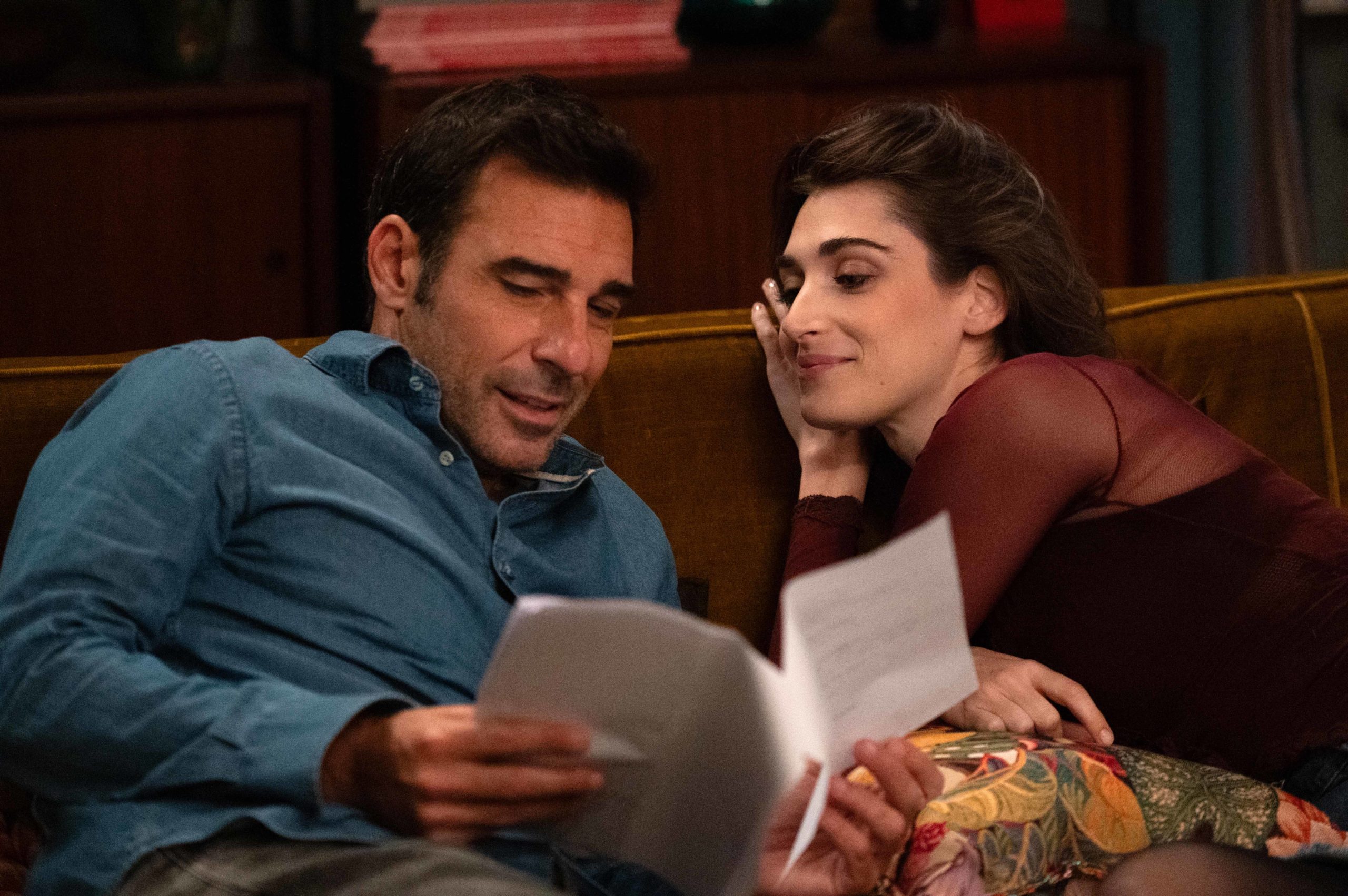 Hlavné postavy filmu Bláznivo (Genovese, 2025) ležia vedľa seba na gauči a čítajú si